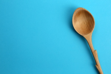 Clean empty wooden spoon on blue background, top view. Space for text