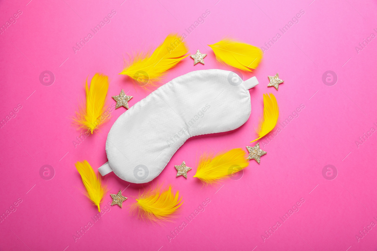 Photo of Soft sleep mask, decorative stars and yellow feather on pink background, flat lay