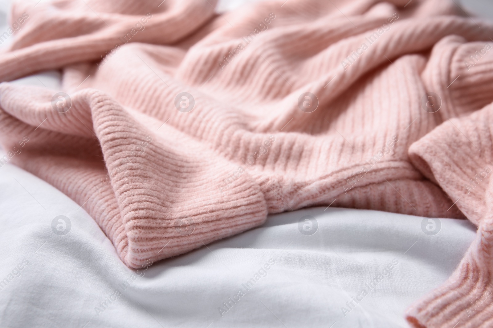 Photo of Pink warm sweater on white crumpled fabric, closeup