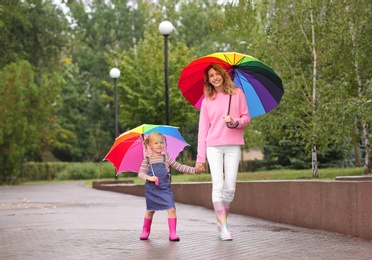Photo of Happy mother and daughter with bright umbrellas walking in park