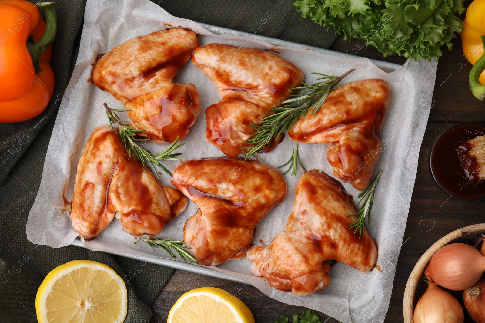 Photo of Flat lay composition with raw marinated chicken wings, rosemary and other products on wooden table