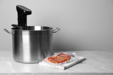 Photo of Thermal immersion circulator in pot and vacuum packing with meat on light grey table, space for text. Sous vide cooking