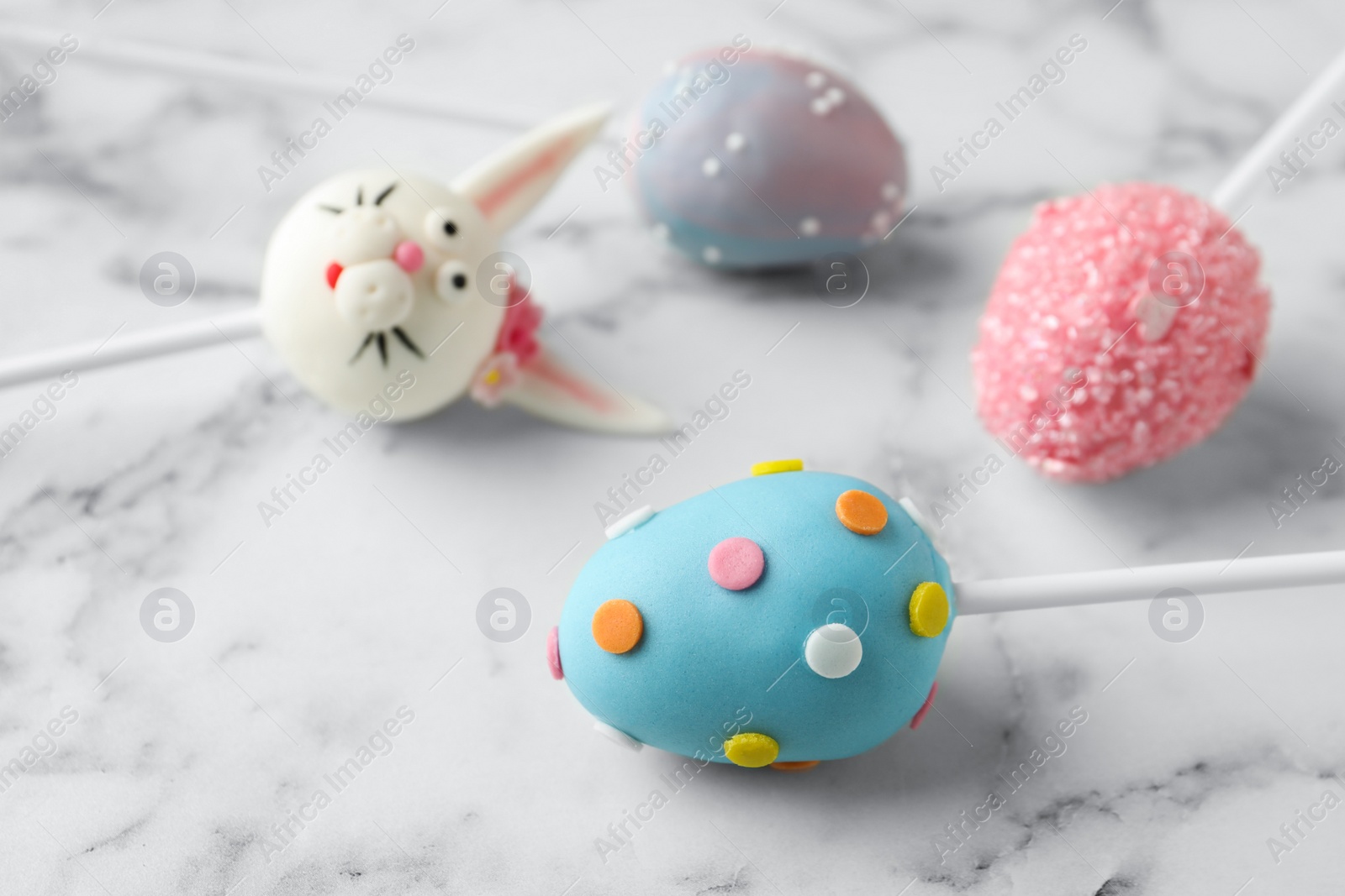 Photo of Delicious sweet cake pops for Easter celebration on white marble table, closeup