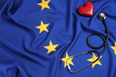 Photo of Stethoscope and red heart on flag of European Union, flat lay. Space for text