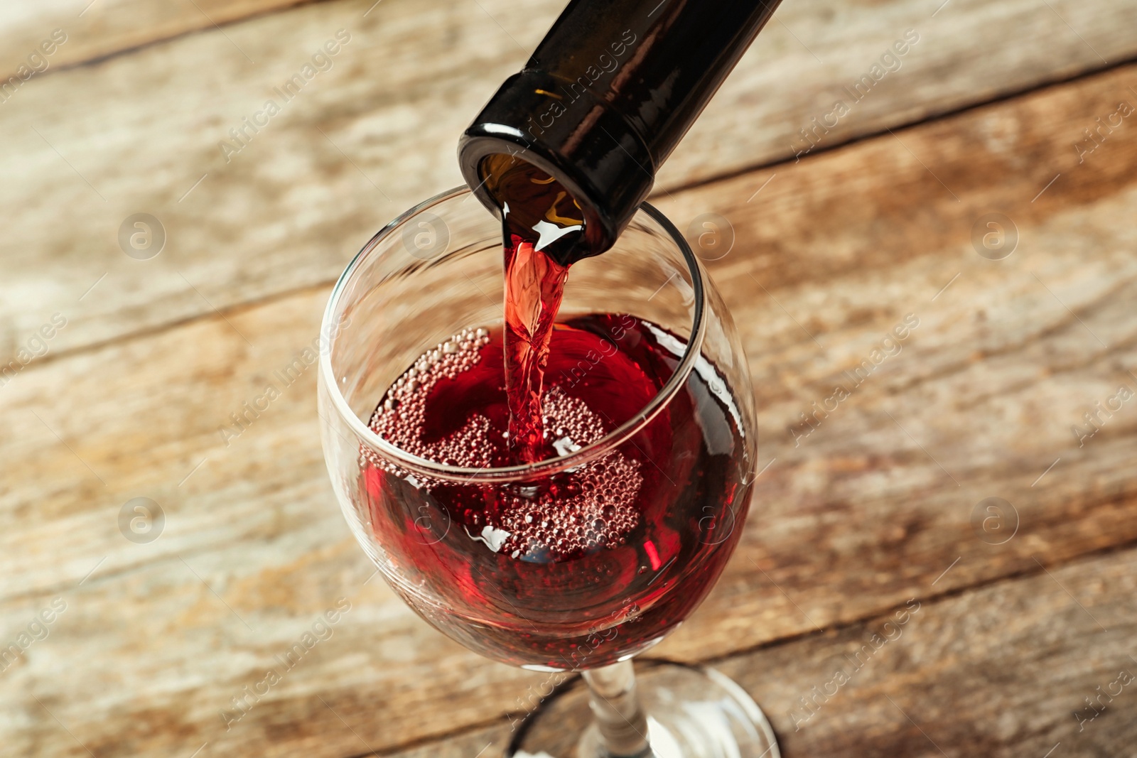 Photo of Pouring delicious red wine into glass on wooden background