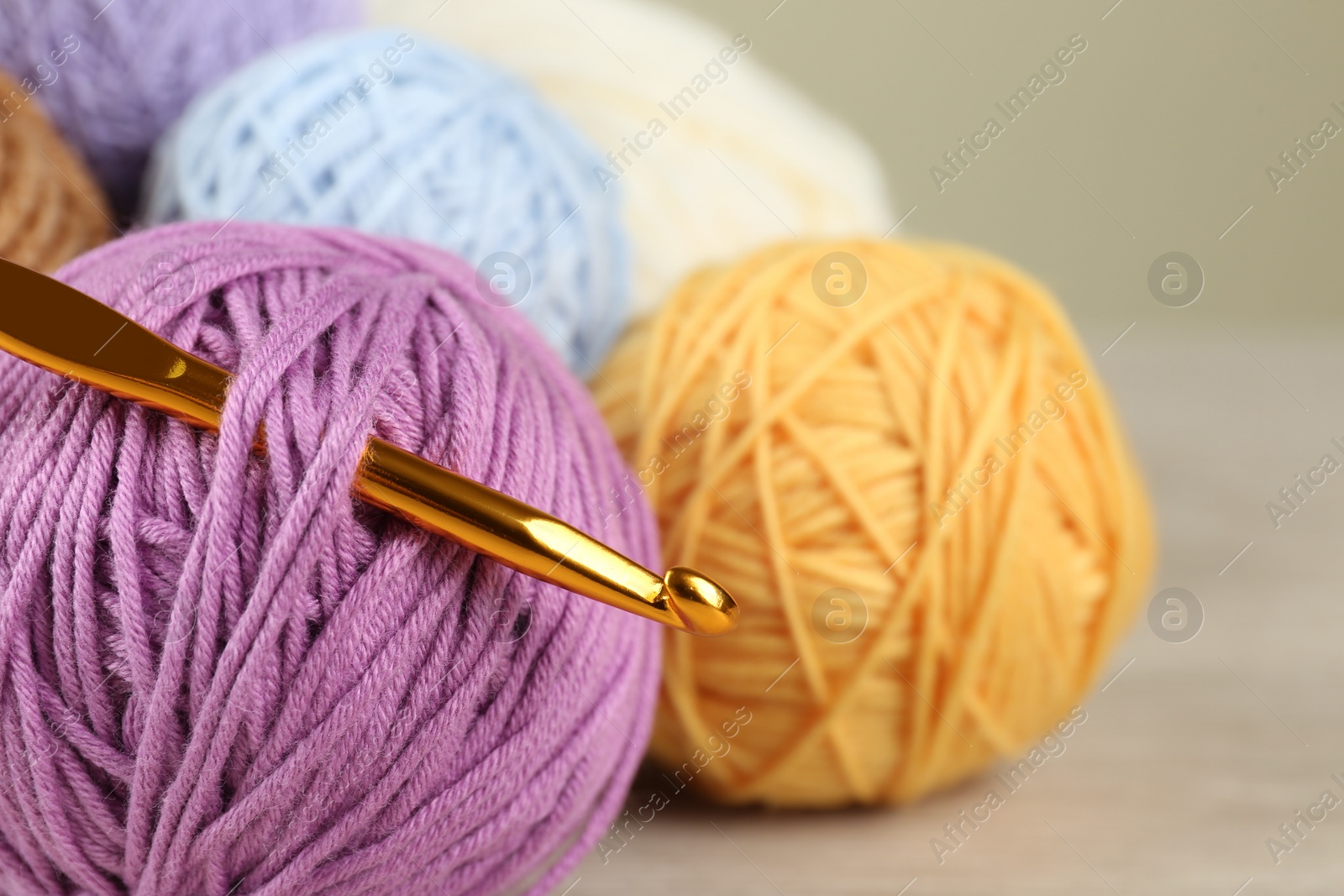 Photo of Clews of colorful knitting threads and crochet hook on wooden table, closeup