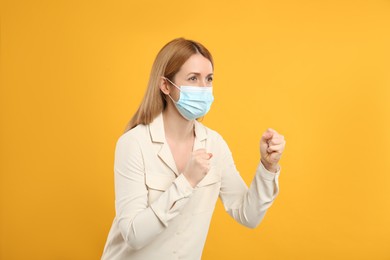 Woman with protective mask in fighting pose on yellow background. Strong immunity concept