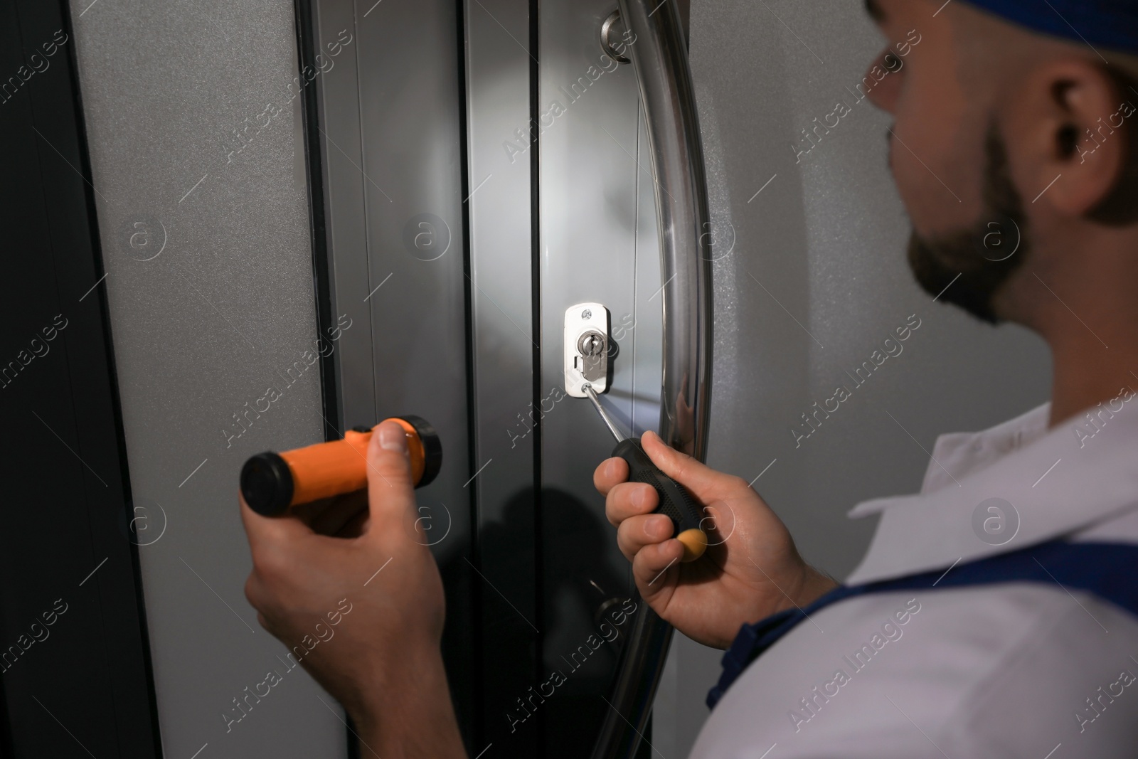 Photo of Repairman with flashlight fixing door lock, closeup