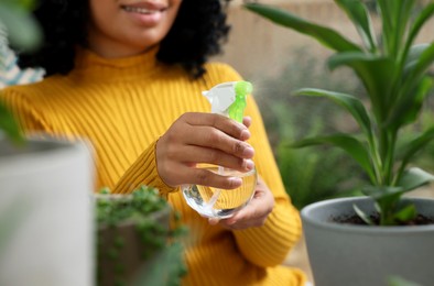 Closeup of happy woman spraying beautiful potted houseplant with water