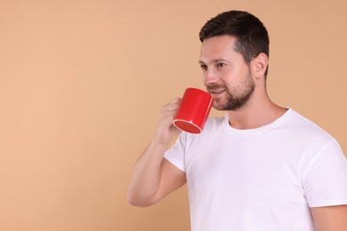 Photo of Man drinking from red mug on beige background. Space for text