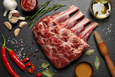 Raw ribs with herbs and spices on black table, flat lay