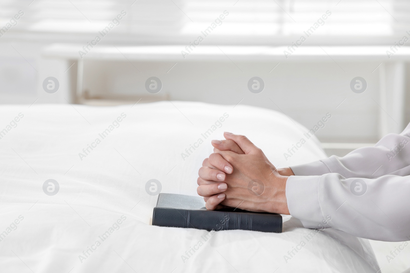 Photo of Religious woman with Bible praying in bedroom, closeup