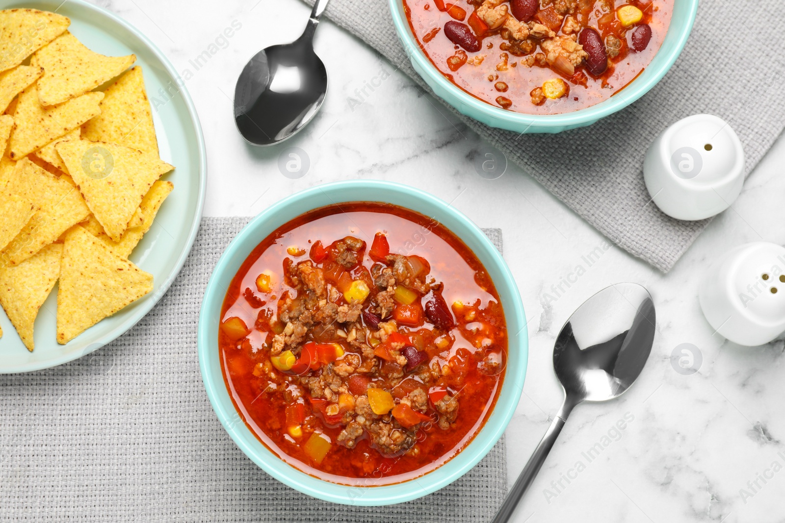 Photo of Tasty chili con carne and tortilla chips on white marble table, flat lay