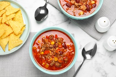 Photo of Tasty chili con carne and tortilla chips on white marble table, flat lay