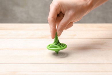 Photo of Woman playing with green spinning top at light wooden table, closeup
