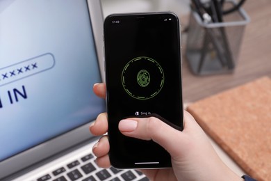 Photo of Woman unlocking smartphone with fingerprint scanner near laptop at workplace, closeup