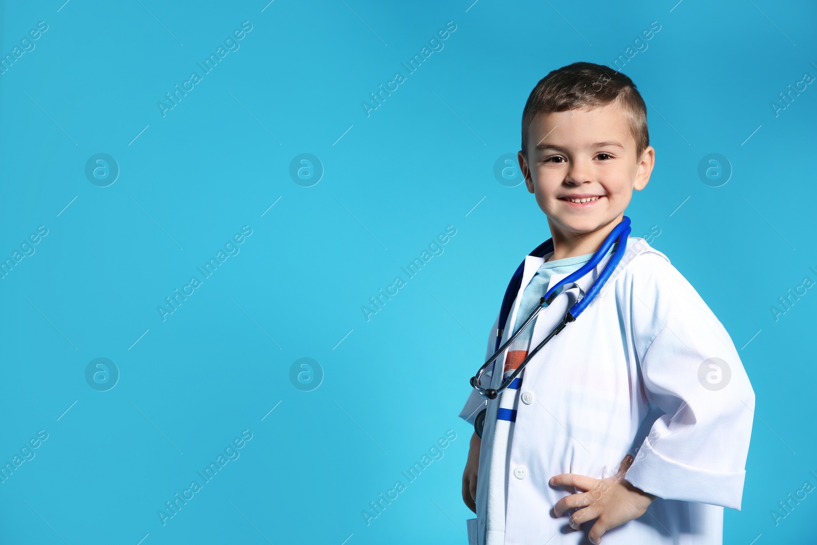 Photo of Cute child in doctor coat with stethoscope on color background. Space for text