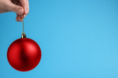 Woman holding red Christmas ball on light blue background, closeup. Space for text