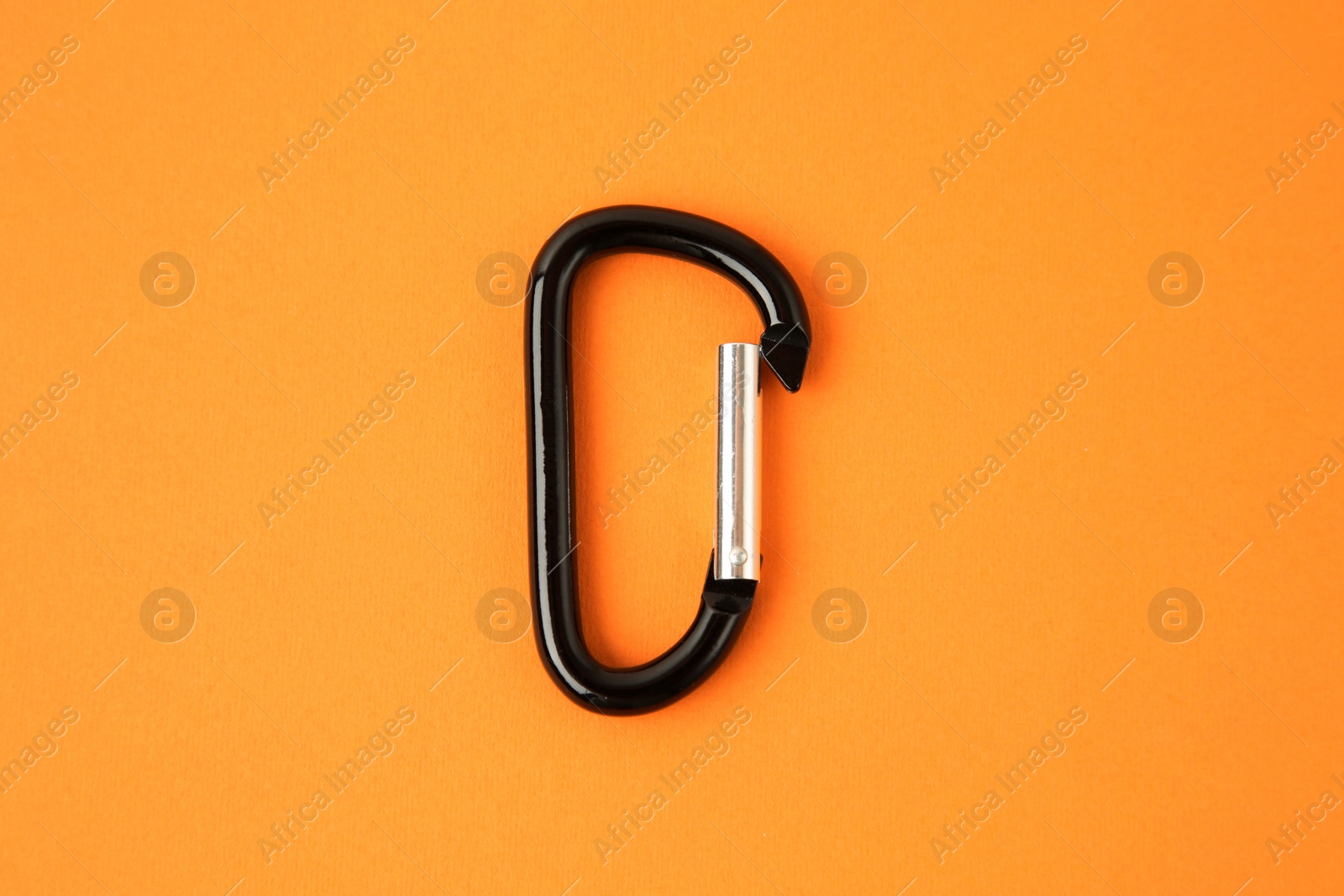 Photo of One black carabiner on orange background, top view