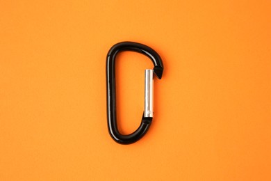 Photo of One black carabiner on orange background, top view