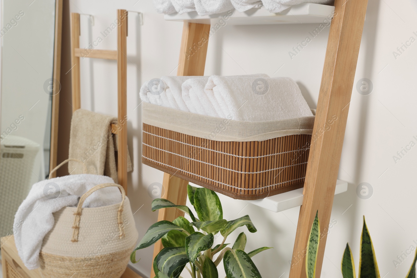 Photo of Soft towels in wicker basket on decorative ladder near white wall