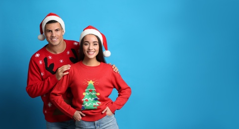 Couple in Christmas sweaters and Santa hats on blue background, space for text