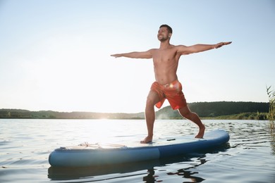 Man practicing yoga on light blue SUP board on river at sunset