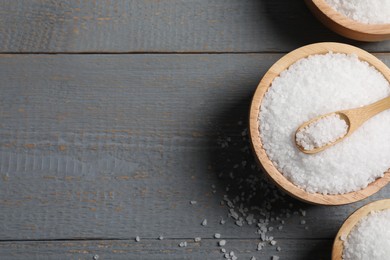 Photo of Bowls of natural sea salt on grey wooden table, flat lay. Space or text