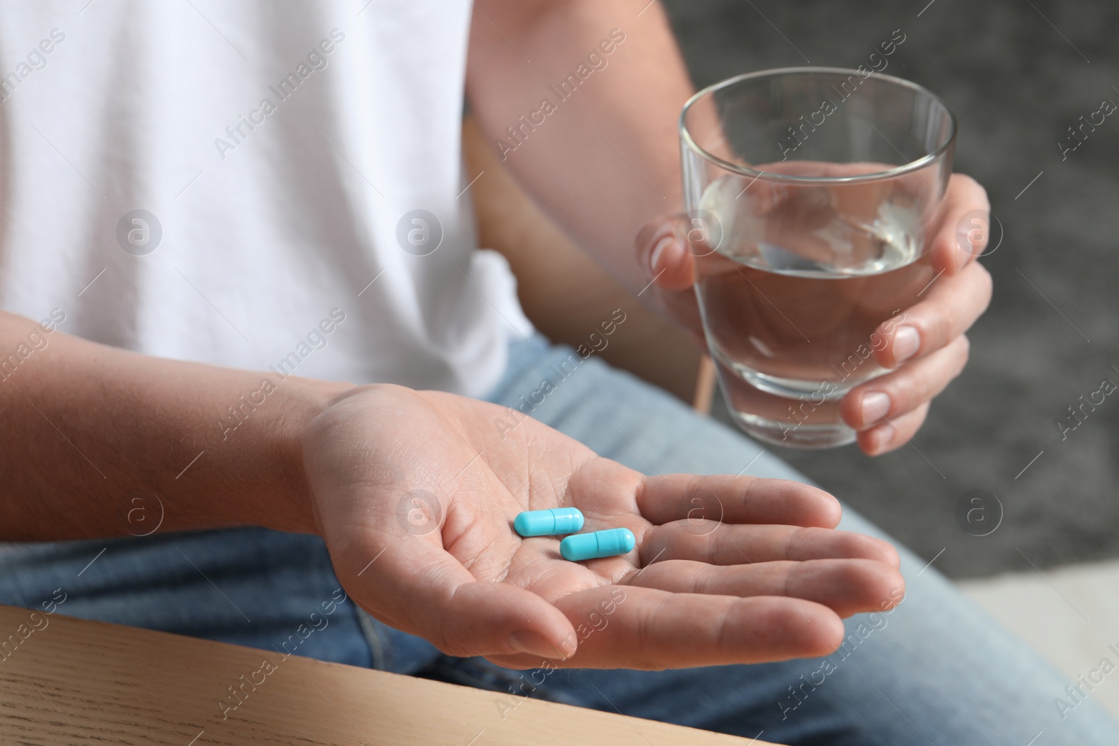 Photo of Man with glass of water and pills on blurred background, closeup