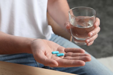 Photo of Man with glass of water and pills on blurred background, closeup