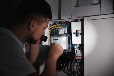 Electrician with flashlight fixing electric panel indoors