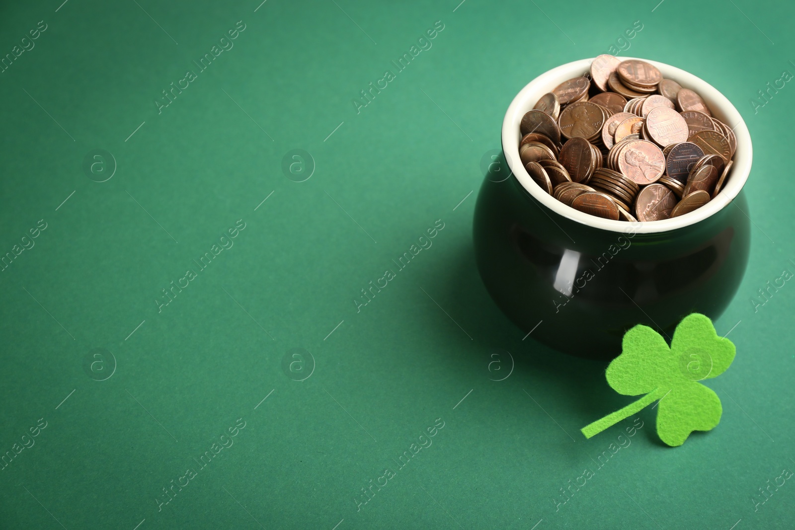 Photo of Pot of gold coins and clover on green background, space for text. St. Patrick's Day celebration