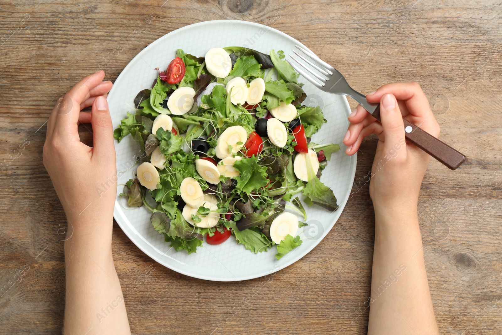 Photo of Woman eating delicious carrot salad at wooden table, top view