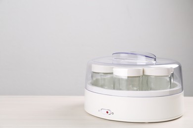 Photo of Modern yogurt maker with empty jars on white wooden table, space for text