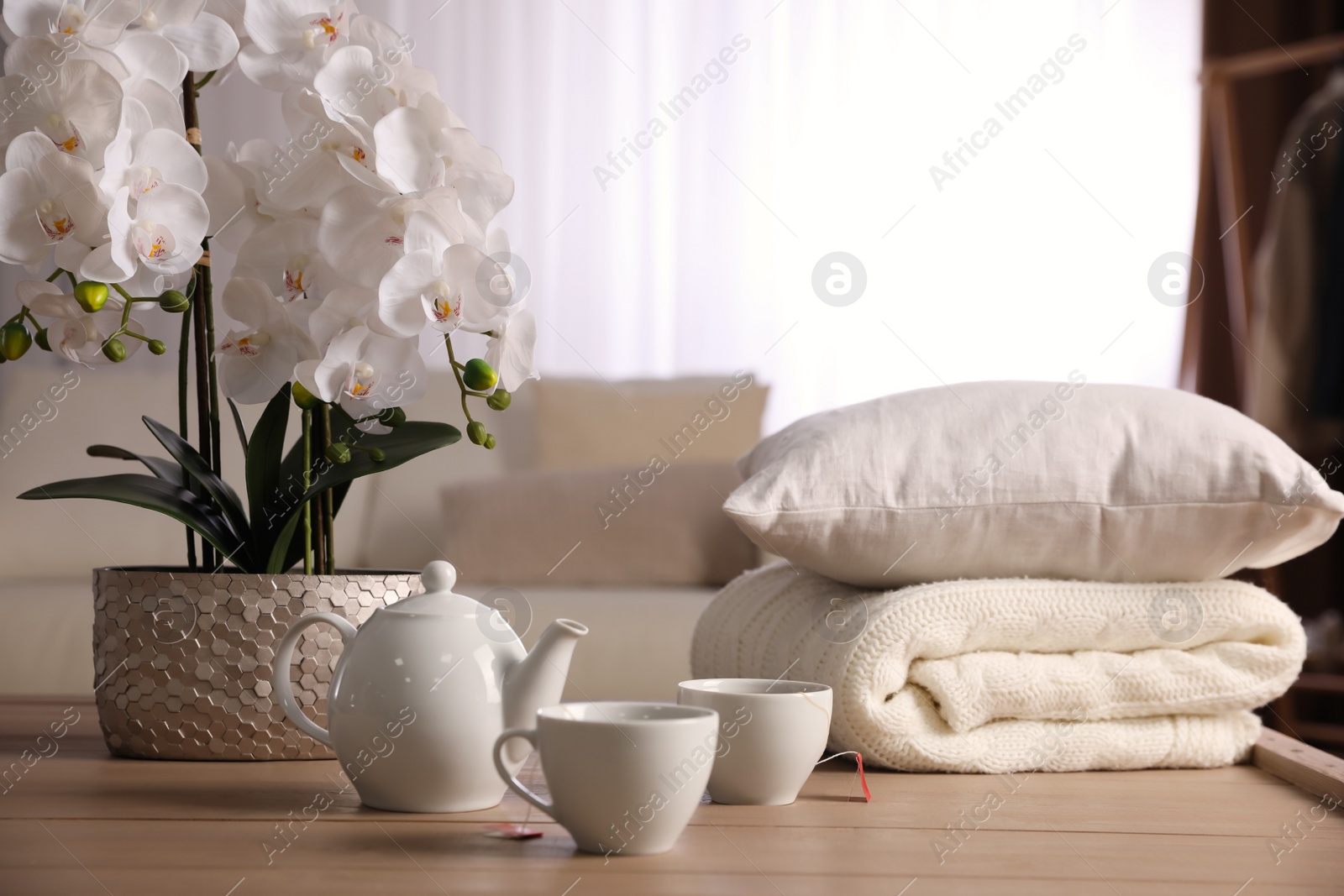 Photo of Beautiful orchid, teapot and cups of tea on table indoors