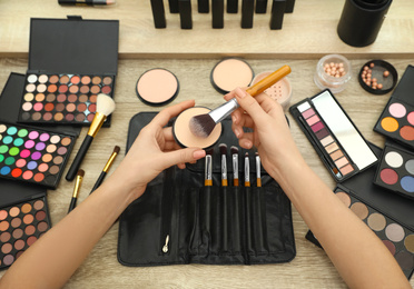 Photo of Professional makeup artist with powder and brush at wooden table, above view