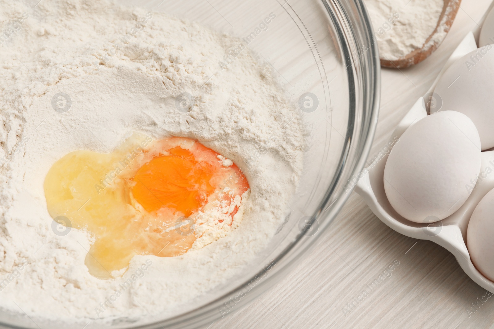 Photo of Bowl with flour and egg on white wooden table, closeup