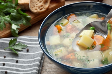 Photo of Spoon of fresh homemade vegetable soup over full bowl on table, closeup