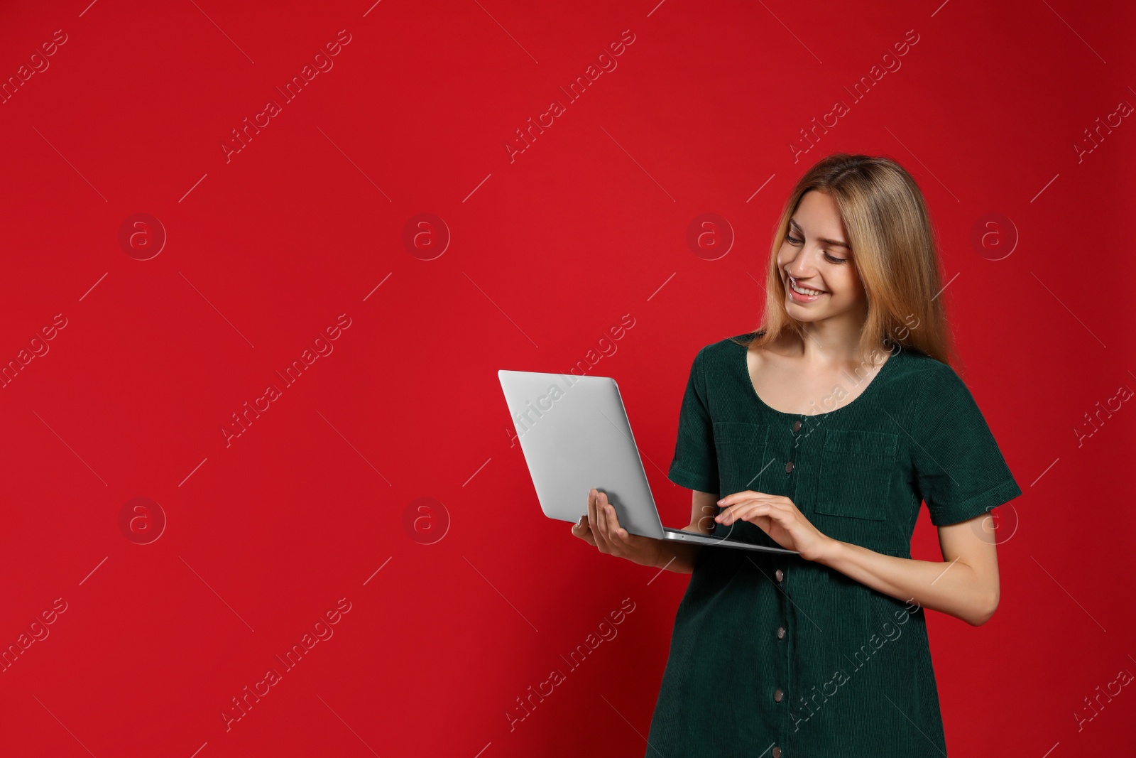 Photo of Portrait of young woman with modern laptop on red background. Space for text