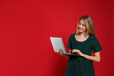 Portrait of young woman with modern laptop on red background. Space for text