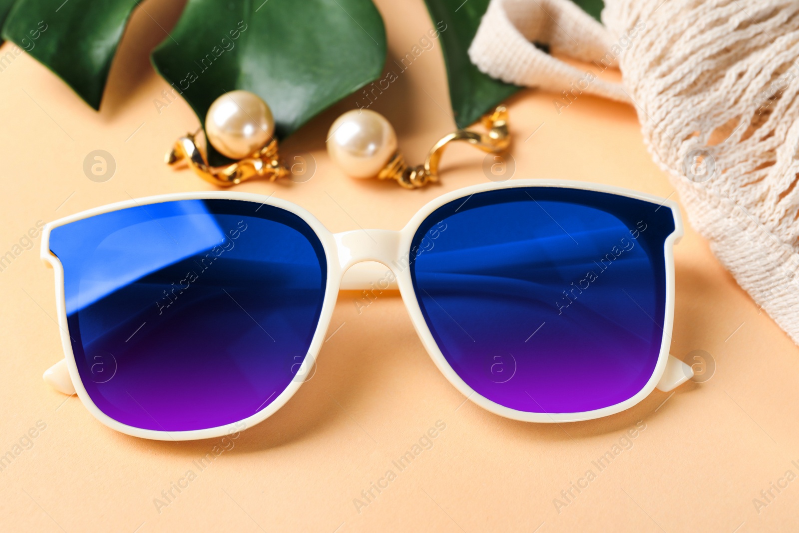 Image of New stylish elegant sunglasses with color lenses on beige background