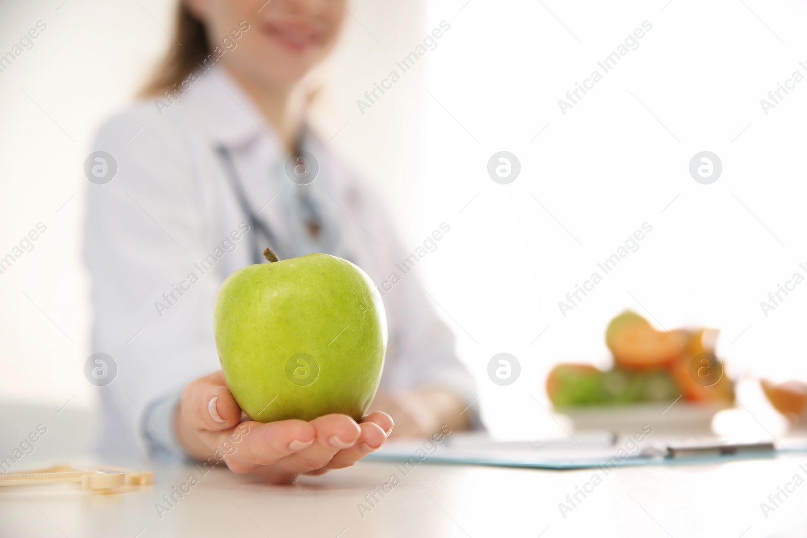 Photo of Nutritionist with apple at desk in office, closeup. Space for text