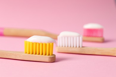 Photo of Wooden brushes with toothpaste on pink background, closeup