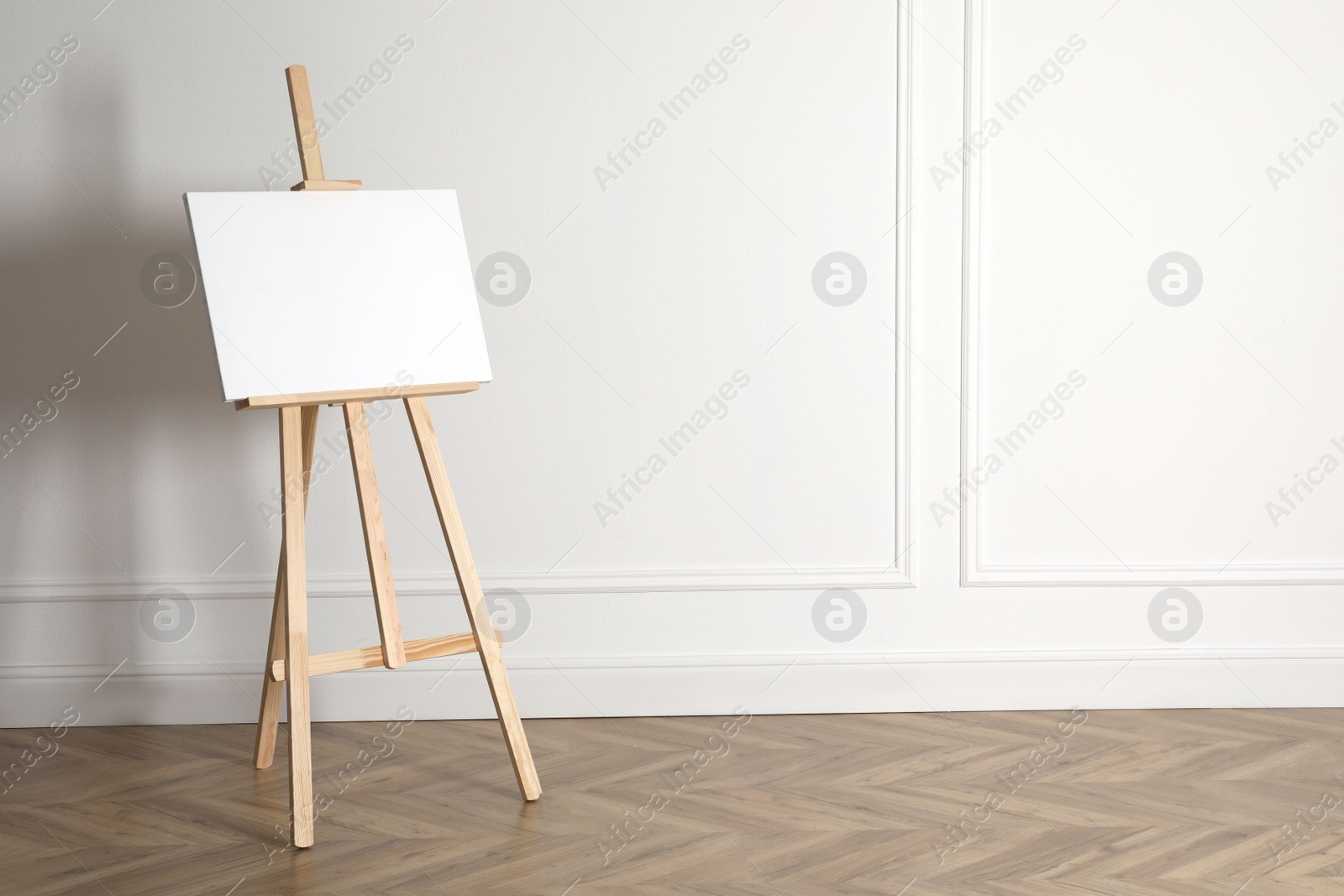 Photo of Wooden easel with blank canvas near light wall. Space for text