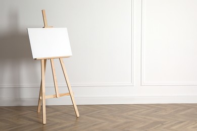 Photo of Wooden easel with blank canvas near light wall. Space for text
