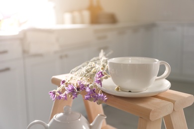 Photo of Decorative ladder with ceramic cup and flowers in kitchen, closeup. Idea for interior design