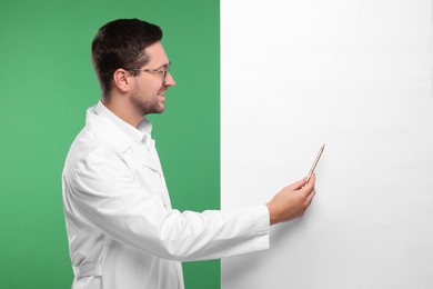 Photo of Ophthalmologist pointing at blank banner on green background, space for text