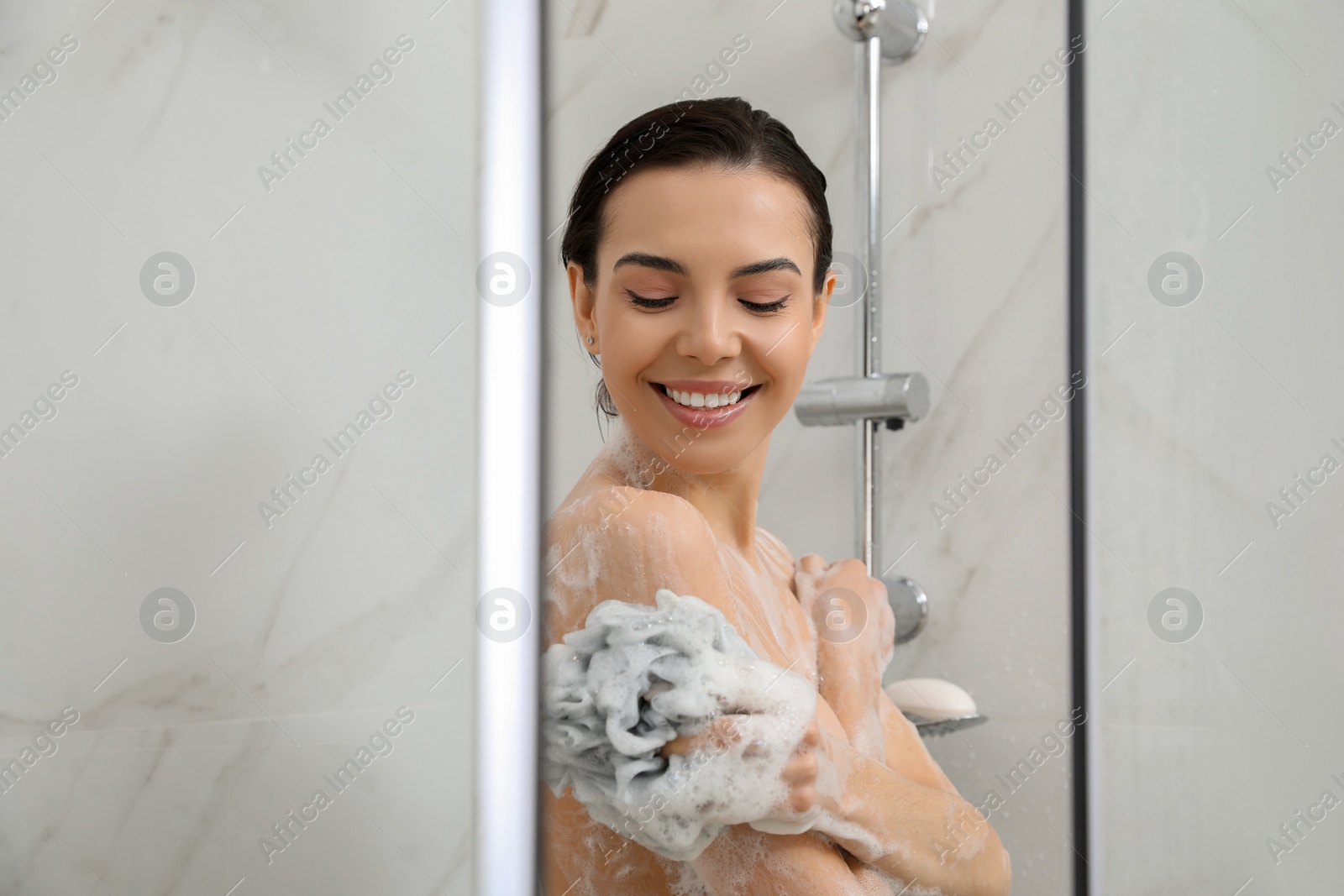 Photo of Young woman with mesh pouf taking shower at home