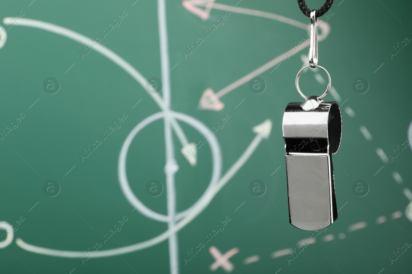 Photo of Referee whistle against green chalkboard with game scheme, closeup. Space for text