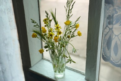 Photo of Bouquet of beautiful wildflowers in glass vase on window sill indoors